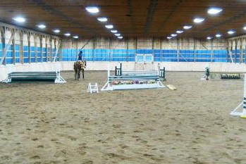 A horse and rider training in a well lit indoor arena.