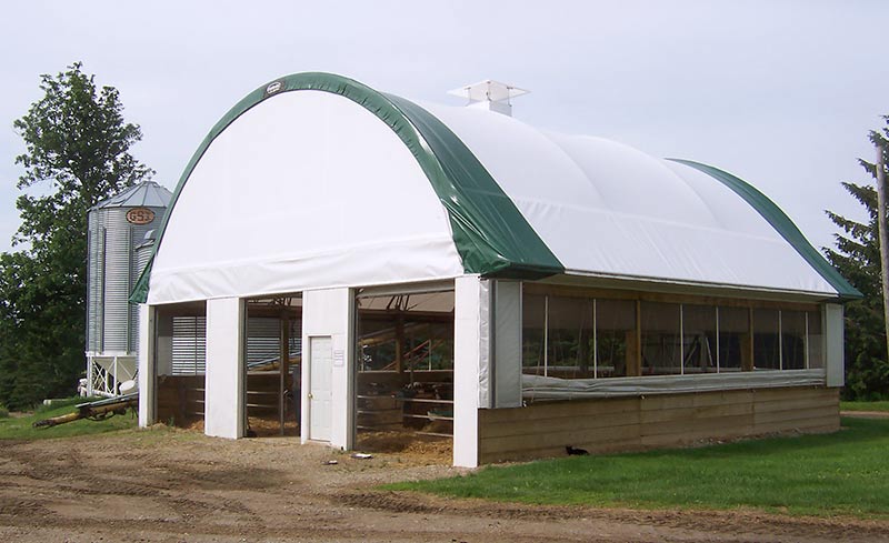 A fabric covered building with open curtain systems along 3 of the walls and a chimney on the ridge.