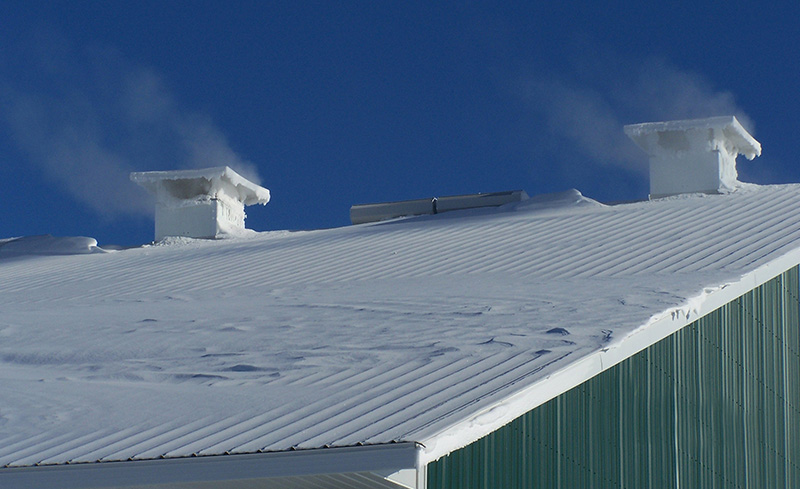 De l'air chaud s'échappe des cheminées de faîtage sur le toit d'une grange enneigée.